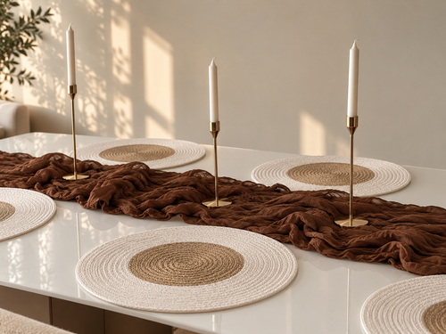 Round two-tone woven placemats with white border and jute centre, styled with a brown linen runner and brass candlesticks on a white table