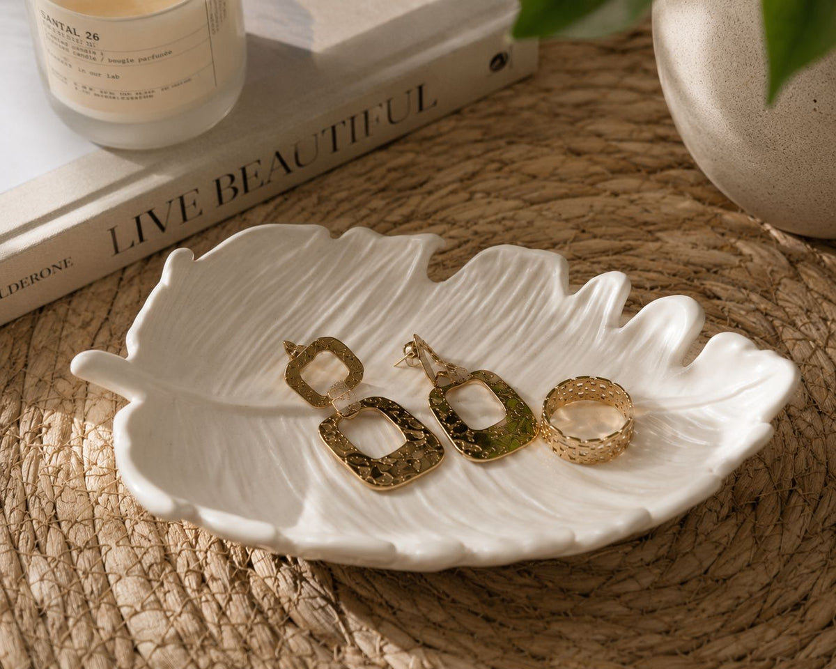 Tropical white leaf tray with gold jewellery on woven placemat