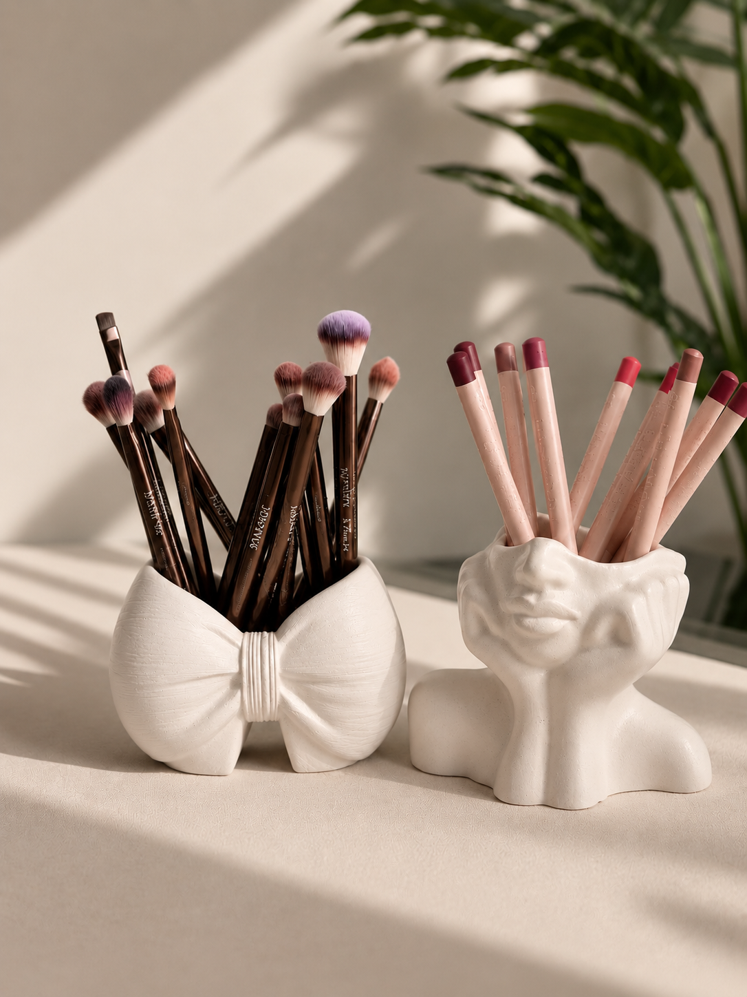 The White Duo — white bow and face bust brush holders styled together on a beige surface