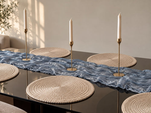 Dining table styled with a baby-blue textured runner, round neutral placemats, and gold-toned candleholders.